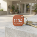 Terracotta 3D-printed society key tag reading 1204 and tap to return, on a bunch of keys at an apartment entrance