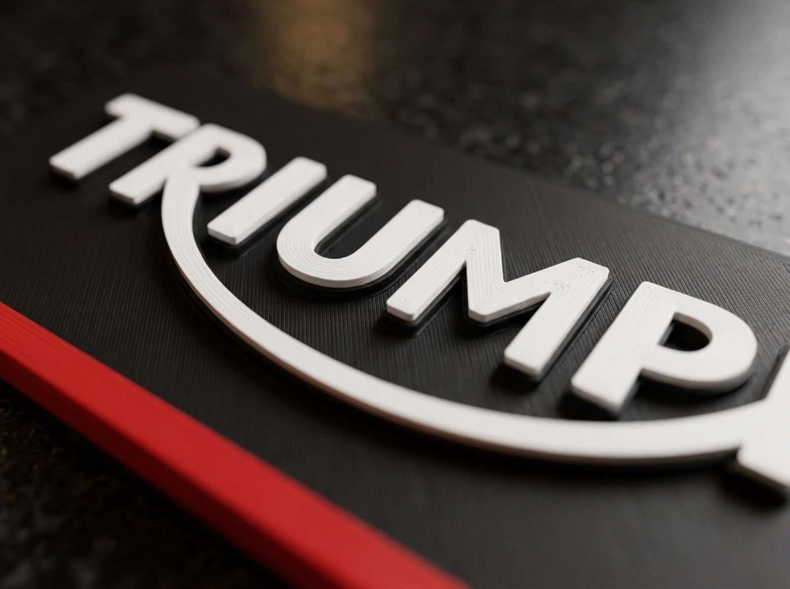 Macro detail of a matte black 3D-printed logo plate with red accent edge